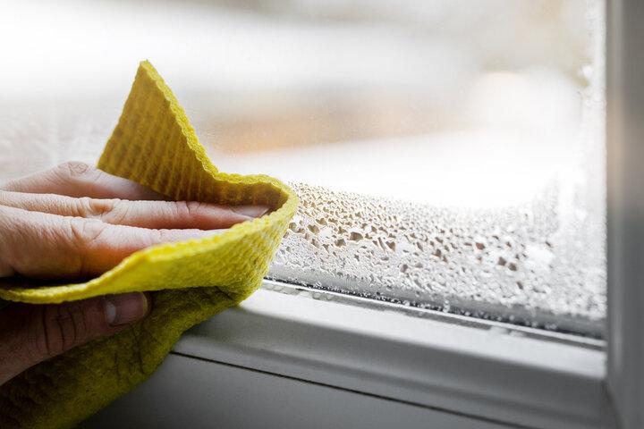 A photograph of someone wiping a window with condensation with a cloth